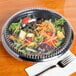 A salad in a Genpak black foam utility bowl with tomatoes and carrots.