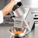 A person using a Hobart food processor to cut carrots in a bowl.