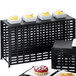 A black metal rectangular lattice riser holding white square containers with cupcakes on a table.