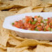 A Fineline Flairware white plastic bowl filled with salsa on a pile of tortilla chips.
