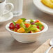 An Acopa ivory stoneware bowl filled with fruit on a table.