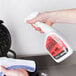 A person using a white spray bottle to clean a waffle iron.