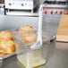 A Winco boar bristle pastry brush in a clear container on a counter with pastries.