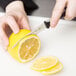 A person's hand using a Dexter-Russell V-Lo scalloped paring knife to slice a lemon.