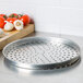 An American Metalcraft heavy weight aluminum pizza pan with holes on it, with garlic and tomatoes on the table.