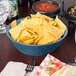 A blue polyethylene large round basket filled with chips on a table with a bowl of salsa.