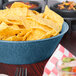 A blue polyethylene round basket filled with tortilla chips on a table.