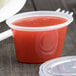 A Newspring oval plastic souffle container with a lid filled with red liquid.
