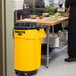 A man standing in a school kitchen next to a Rubbermaid yellow trash can.