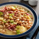 A bowl of Furmano's Great Northern Beans and ham with a spoon on a white table.