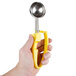 A hand holding a yellow and silver scoop with a yellow handle.