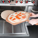 A person using an American Metalcraft natural pressed pizza peel to put a pizza in the oven.