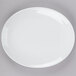 A Tuxton bright white oval china platter with a white rim on a gray surface.