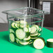 A Cambro clear polycarbonate food pan with sliced cucumbers in it on a green surface.
