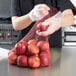 A person in gloves putting red apples into a Royal Paper red plastic mesh bag.