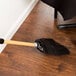 A Carlisle 6-stitch janitor corn broom with a wooden handle on a wood floor.