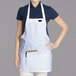 A woman wearing a white Chef Revival apron with a black pocket.