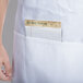A person's hand holding a note in the pocket of a white Chef Revival bib apron.