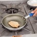 A person frying chicken in a Vollrath aluminum non-stick fry pan with a blue handle.