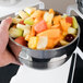 A person holding a Vollrath stainless steel serving bowl filled with fruit.