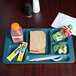 A teal Cambro 6 compartment tray with a sandwich, a drink, and a piece of broccoli on it.