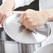 A hand holding a Vollrath Lincoln metal lid over a pot.