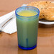 A blue Cambro plastic tumbler filled with green juice next to a plate of bagel