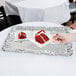 A hand holding a piece of red velvet cake on a white Victorian metal tray.