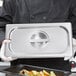A person holding a Vollrath stainless steel slotted steam table pan cover filled with food.