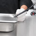 A person in white gloves using a black tool to hold a Vollrath stainless steel slotted pan cover over a metal container.