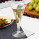 A clear plastic champagne flute filled with champagne sits on a table next to a plate of grapes.