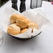 A basket of rolls on a table with a white linen-like napkin.