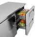 A stainless steel drawer with trays of vegetables in a Turbo Air undercounter refrigerator.