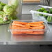 A Rubbermaid clear plastic food storage box full of carrots on a counter.