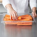 A person reaching for carrots in a Rubbermaid clear polycarbonate food storage container.