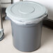 A grey Continental Huskee round trash can lid on a grey trash can with a plastic bag.