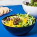 A Fineline black plastic bowl filled with salad on a blue table.