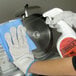 A gloved hand cleaning a circular meat slicer blade.
