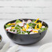 A bowl of salad with vegetables in a black Fineline bowl.