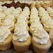 A tray of white fluted cupcakes with white frosting on a counter in a bakery display.