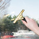 A hand using a Unger brass window squeegee to clean a window.
