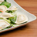 A square ivory melamine platter with salad and dumplings on it.