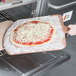 A person using an American Metalcraft square pizza peel to put a pizza with cheese in the oven.