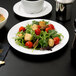 A white porcelain salad plate with salad, tomatoes, and croutons on a black surface.