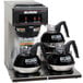 A Bunn low profile pourover coffee maker on a counter with three coffee pots.