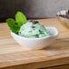 A white ceramic American Metalcraft sauce cup filled with mint chocolate chip ice cream and garnished with mint leaves and chocolate chips.