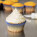 A close up of a yellow cupcake with white frosting in a blue striped baking cup.