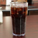 A Carlisle clear plastic tumbler filled with brown soda and ice on a table.