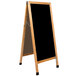 An Aarco oak A-frame sign board with black marker board on a black board with wooden legs.