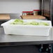 A white Carlisle food storage container filled with lettuce.